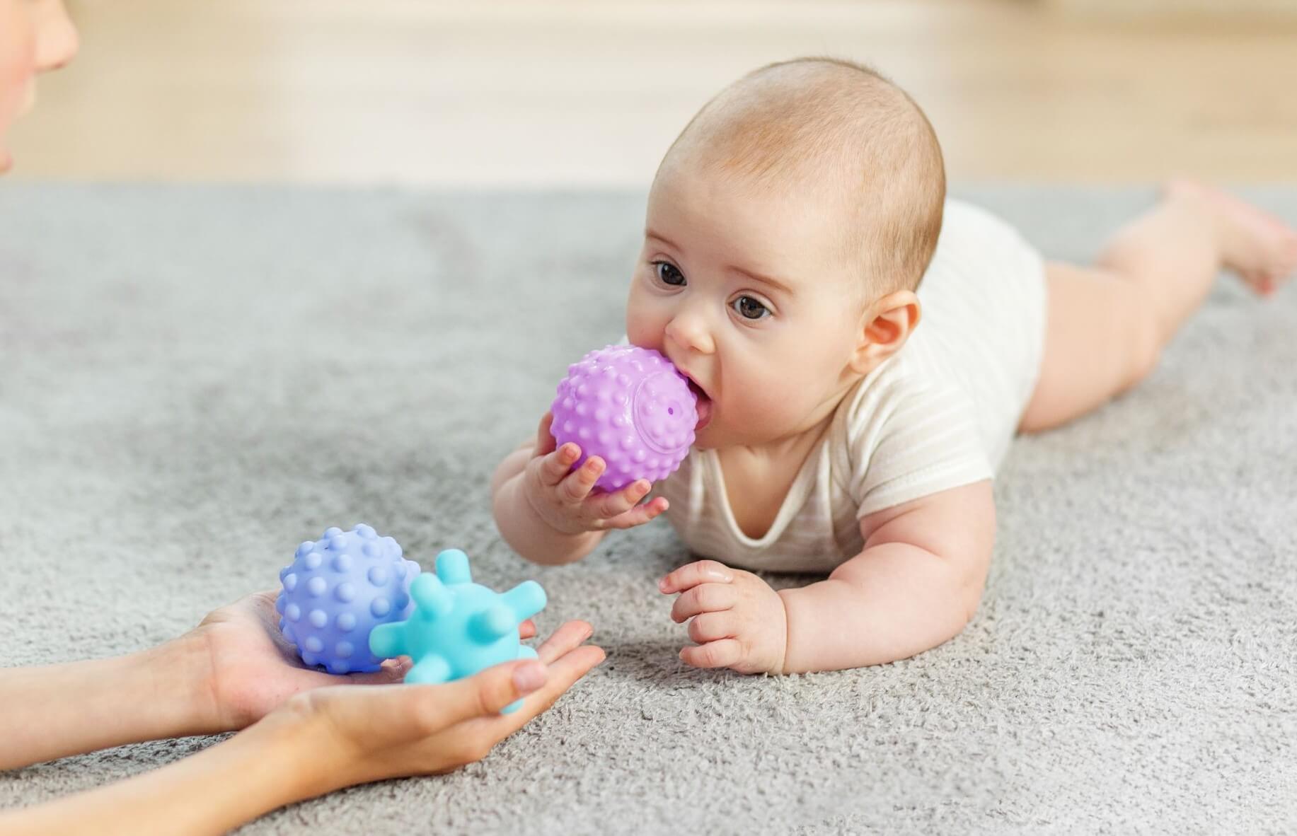 Bébé en tummy time explorant une balle sensorielle avec sa maman