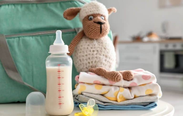 Biberon de lait, doudou mouton, vêtements de rechange et tétine disposés devant un sac à langer vert