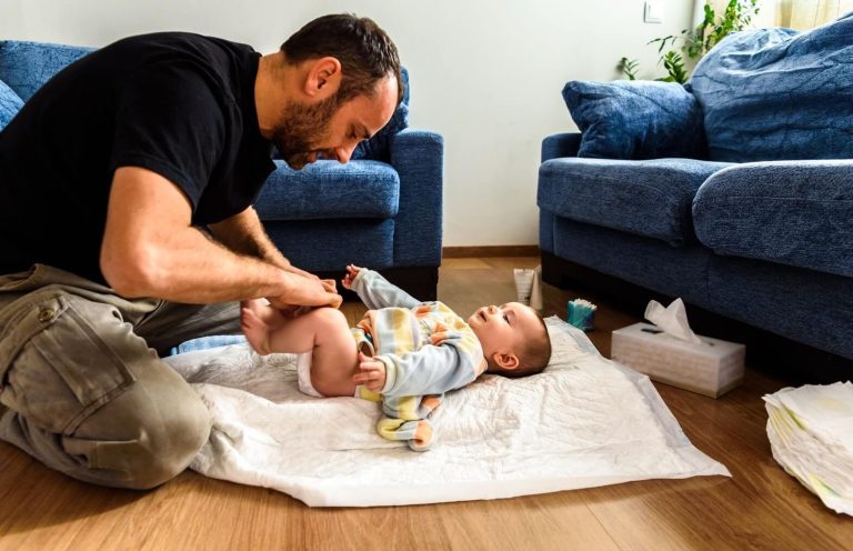 Papa changeant son bébé au sol dans le salon sur un tapis de change