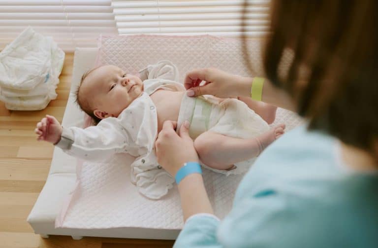 Maman changeant son bébé sur une table à langer à la maison avec lumière naturelle