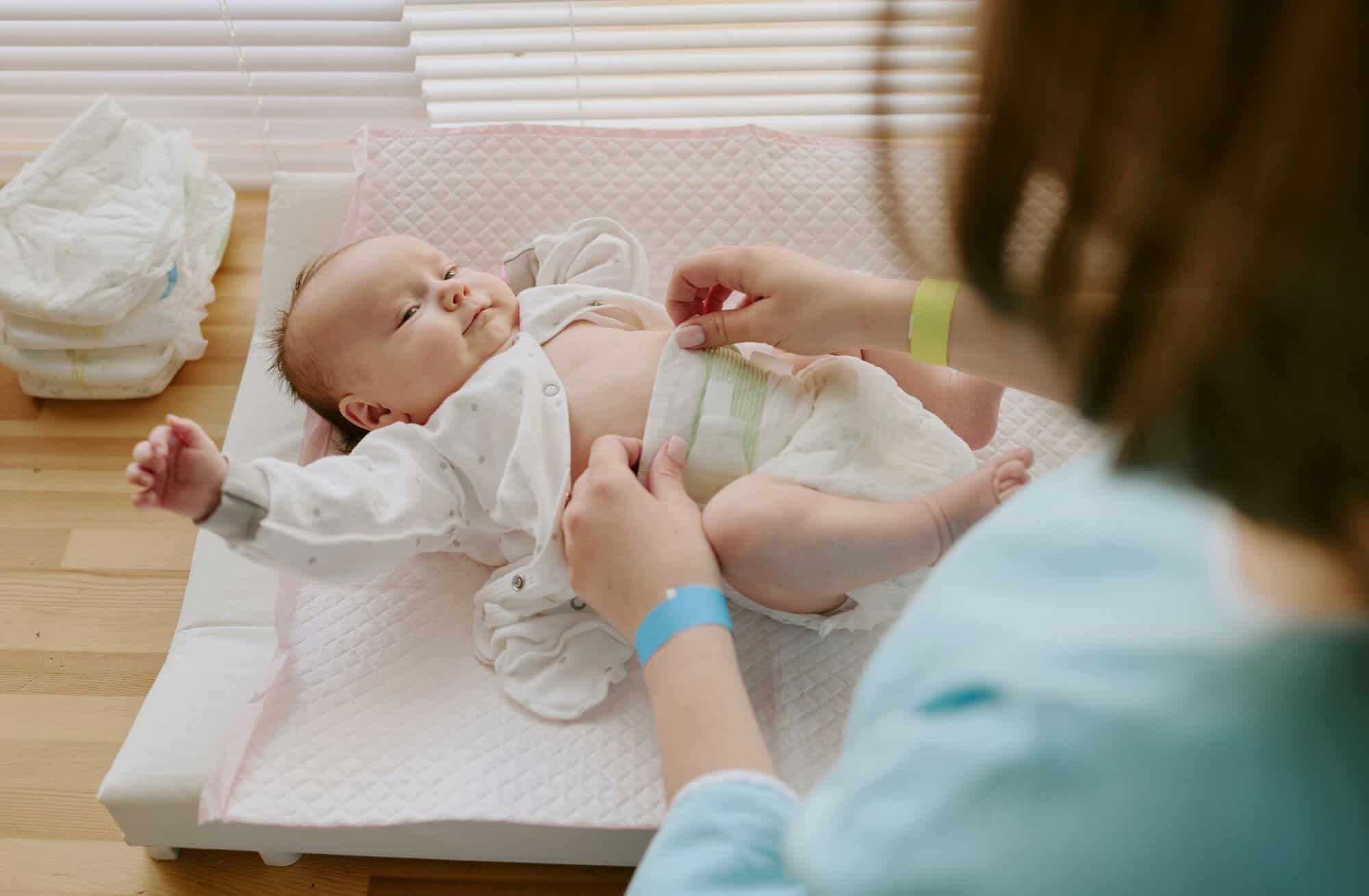Maman changeant son bébé sur une table à langer à la maison avec lumière naturelle