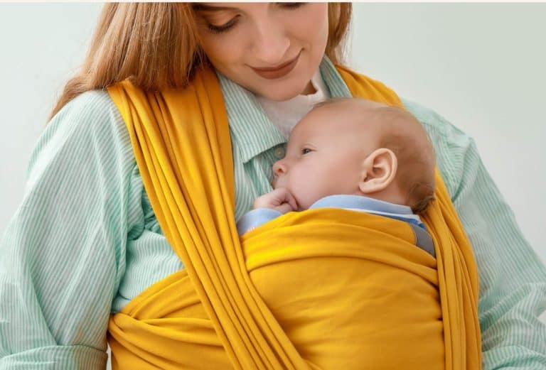 Nouveau-né porté contre sa maman dans une écharpe élastique jaune, illustrant la position physiologique et le portage cocon