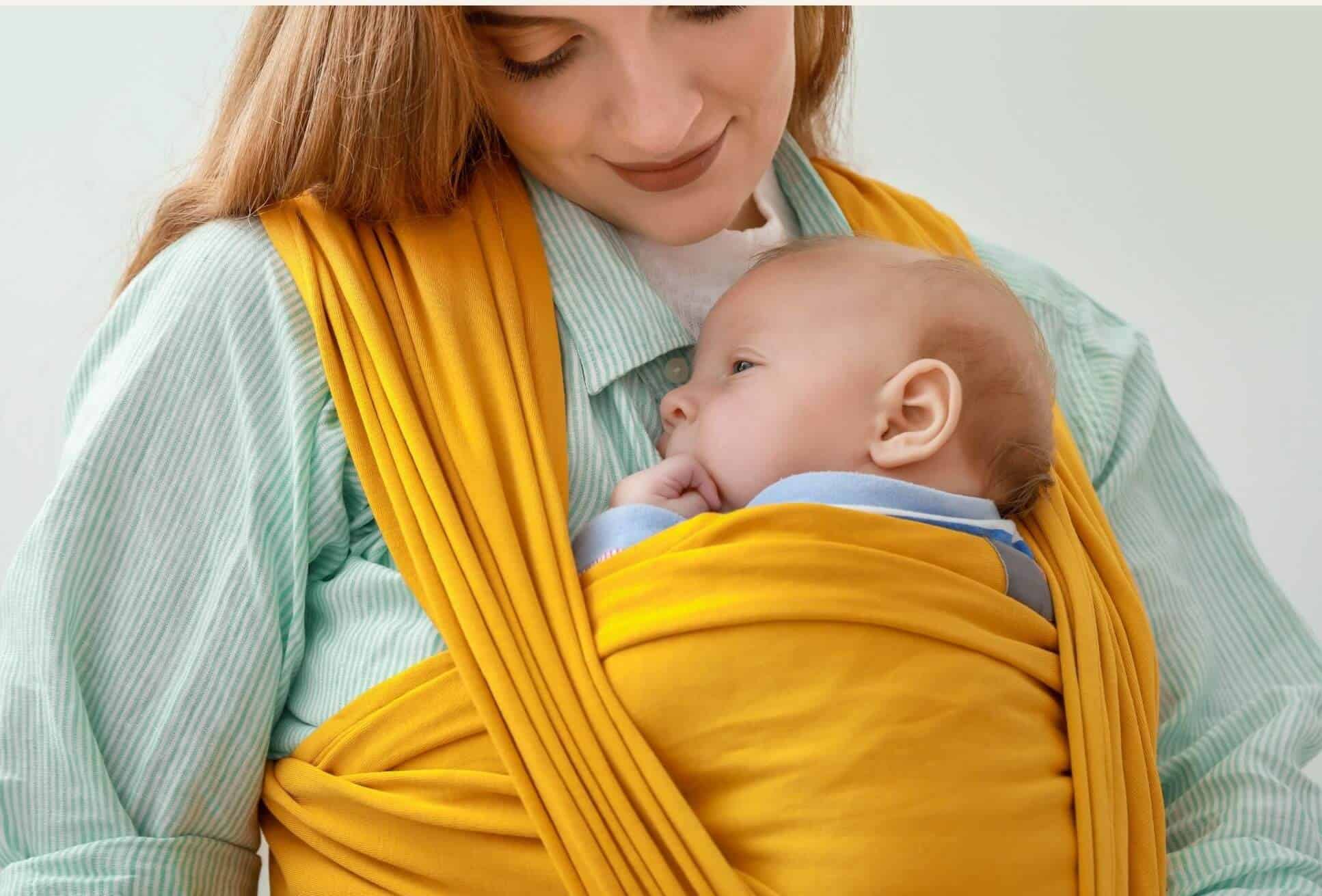 Nouveau-né porté contre sa maman dans une écharpe élastique jaune, illustrant la position physiologique et le portage cocon