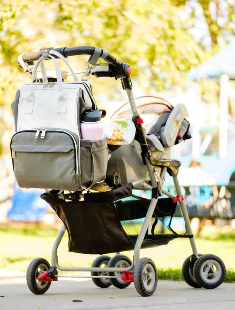 Sac à langer blanc accroché à une poussette lors d'une sortie en extérieur avec bébé