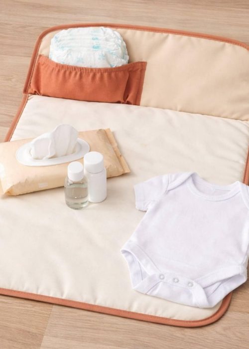 Matelas à langer nomade déplié avec couche, lingettes, body blanc et produits de change pour bébé