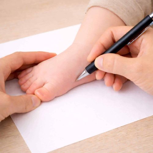 Parent qui trace le contour du pied de son bébé sur une feuille pour mesurer la pointure